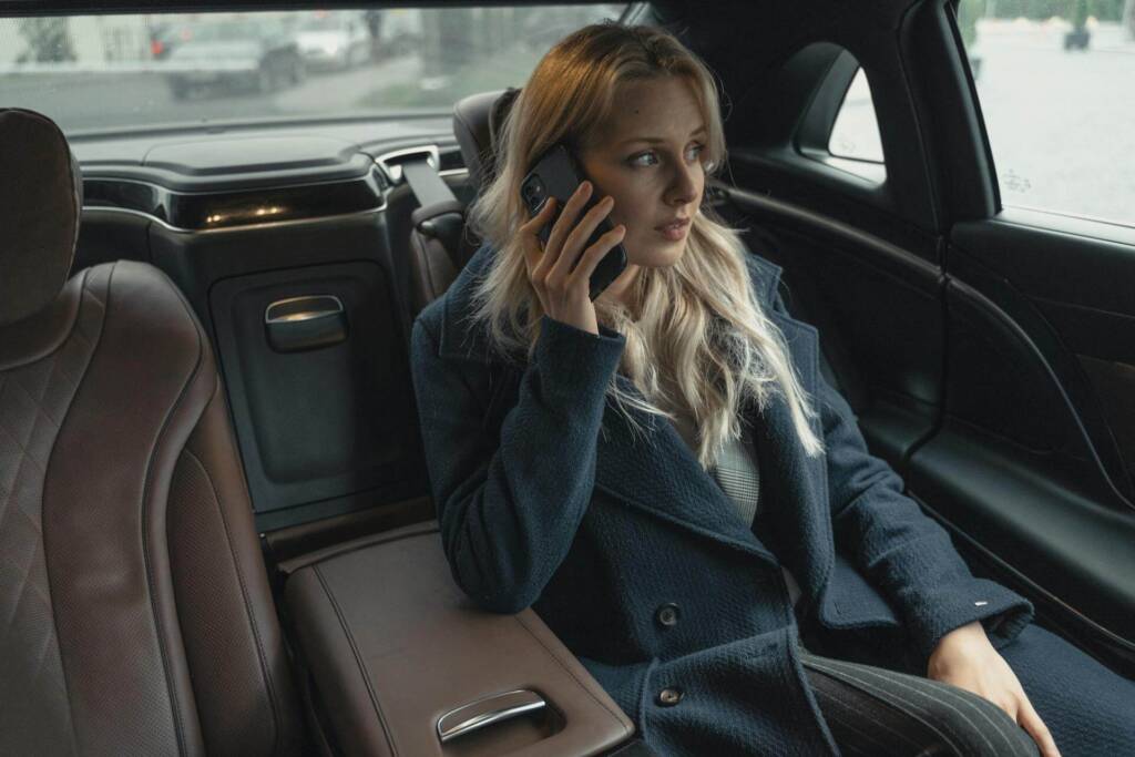 A businesswoman seated comfortably in a luxury minicab, dressed professionally. The interior of the vehicle is sleek and elegant, offering a premium travel experience.